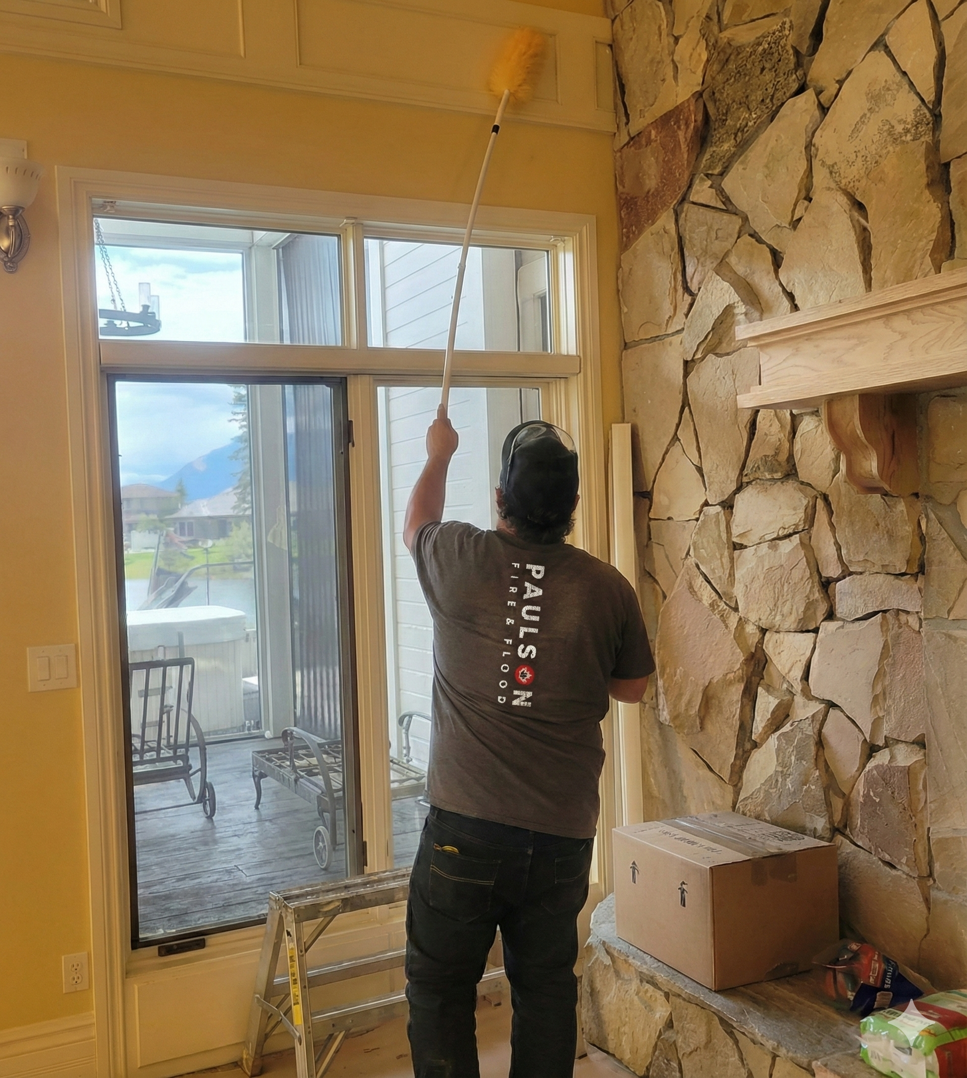 Restoration technician cleaning high interior walls with an extension duster inside a home affected by fire or smoke damage.